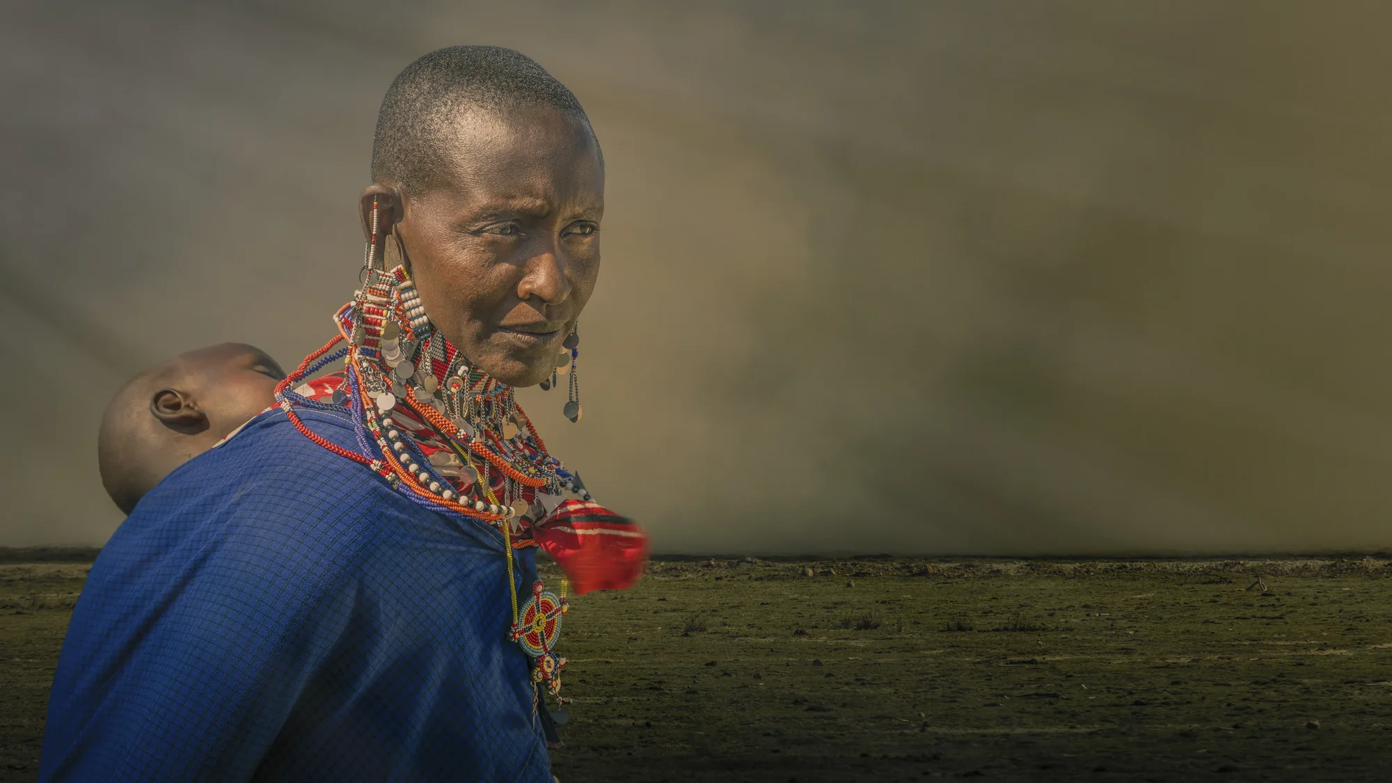 A Maasai mother carrying her child in the East African landscape